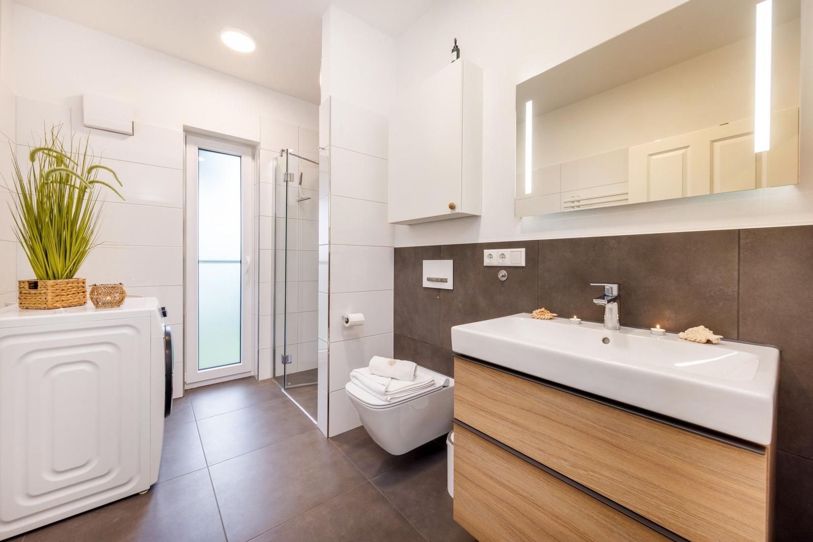 Badezimmer mit Waschmaschine, Dusche und Waschtisch mit Spiegel.