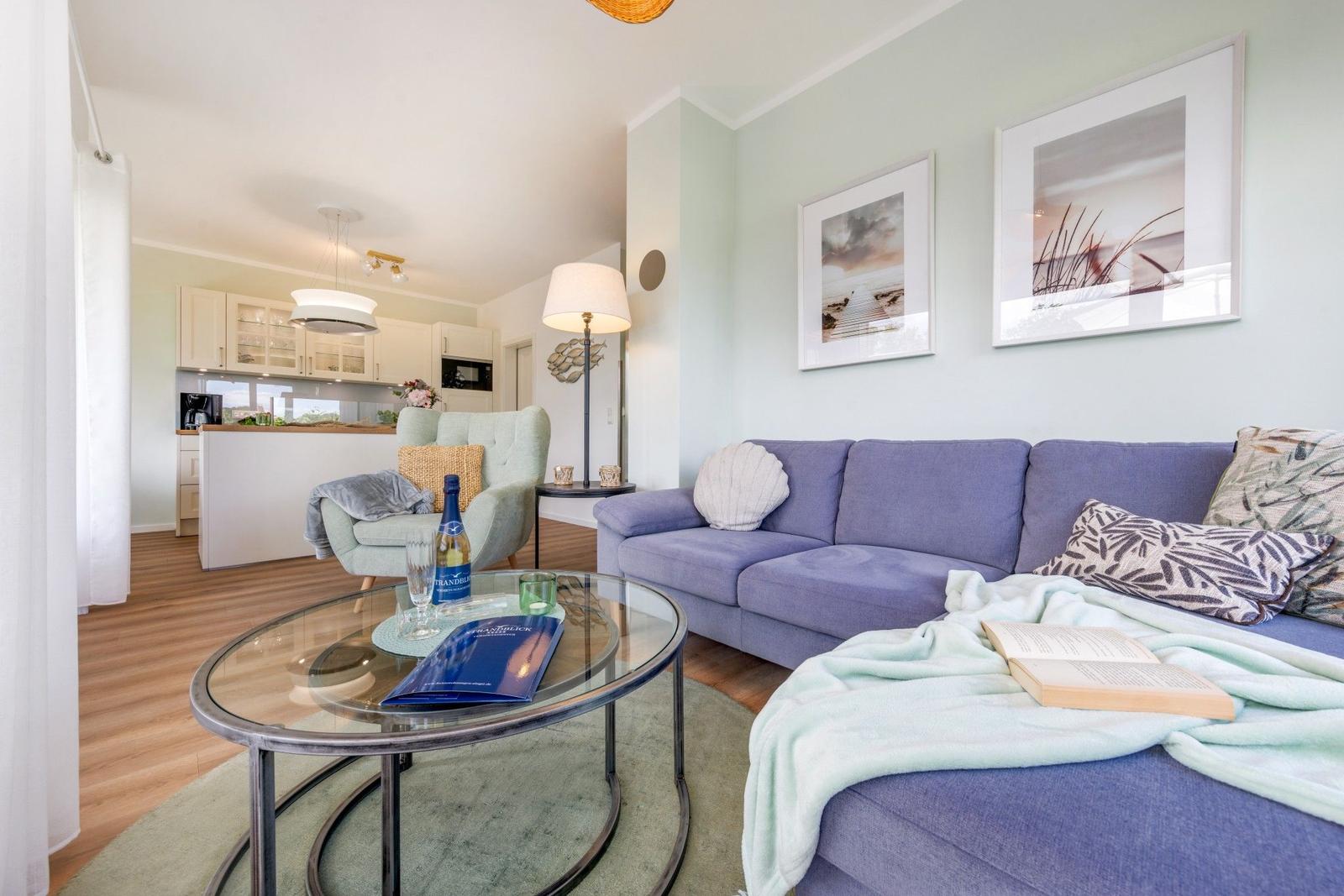 Lounge mit Sofa, Couchtisch und Blick in die Küche.