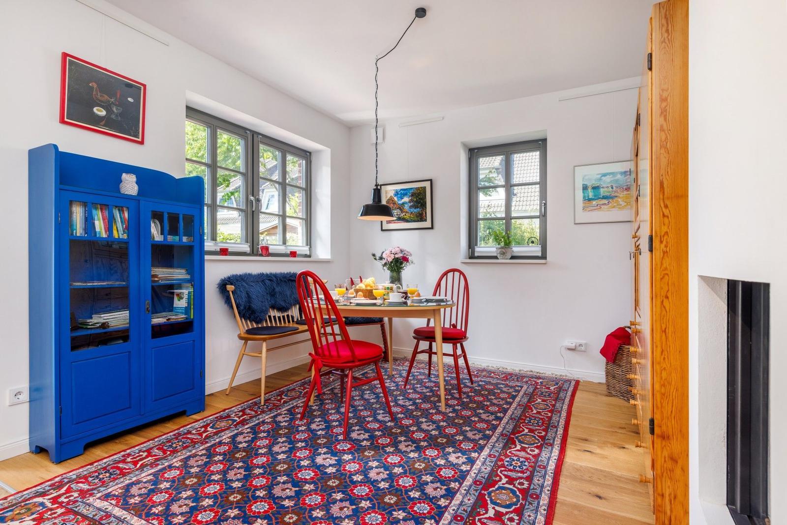 Esszimmer mit blauem Bücherregal, roten Stühlen und buntem Teppich.