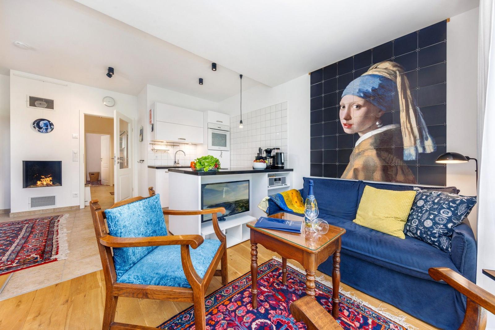 Wohnzimmer mit Sofa, Stuhl und Küchenbereich. Wandbild von Mädchen mit Perlenohr.