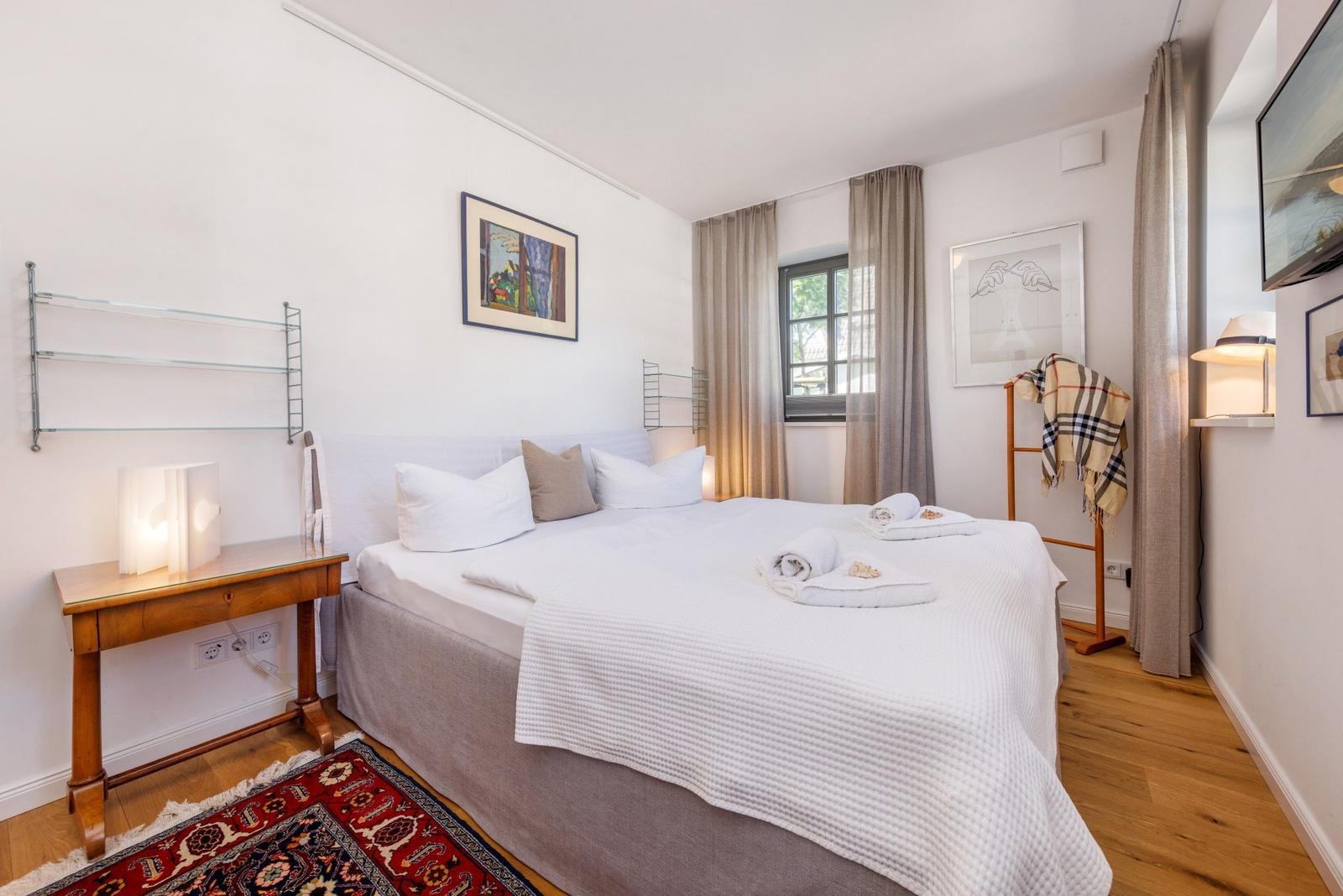 Ein Schlafzimmer mit Bett, Fenster, Schreibtisch und Wandbildern.