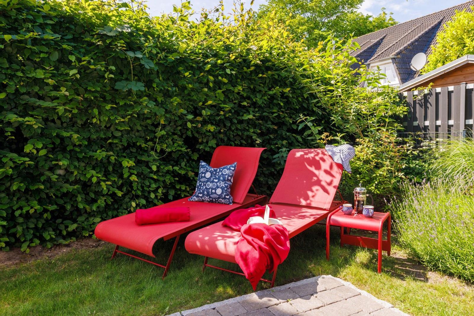 Zwei rote Liegestühle mit Kissen und Tisch im Garten neben Hecke und Lavendel.