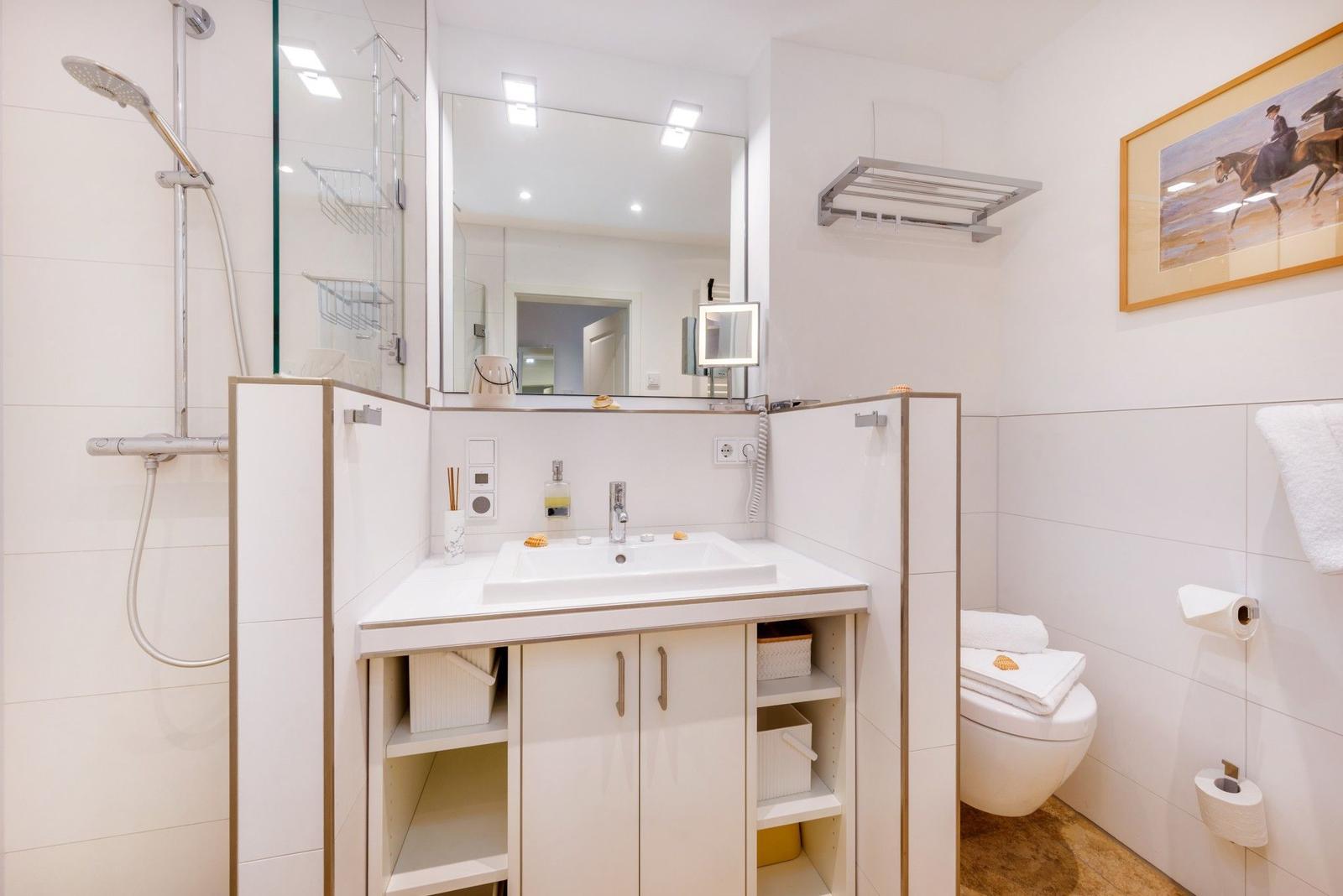 Badezimmer mit Dusche, Waschbecken und Toilette. Weiße Fliesen und moderne Einrichtung.