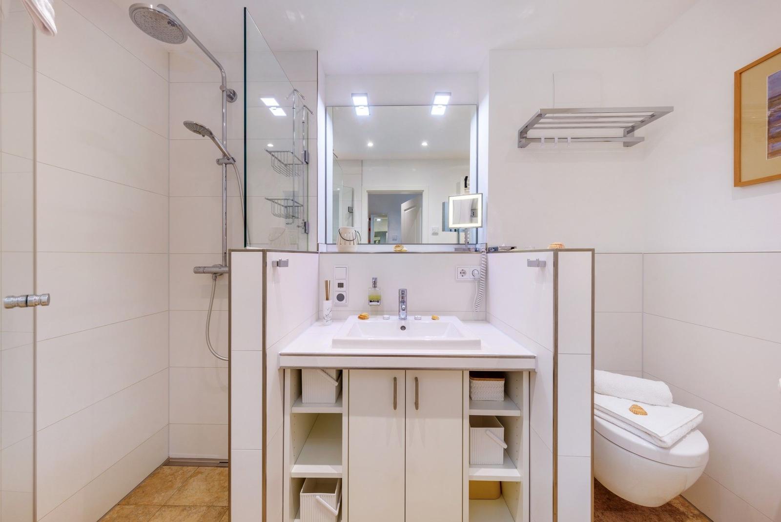 Badezimmer mit Dusche, Waschbecken und Toilette. Fliesenwand und Spiegel sichtbar.
