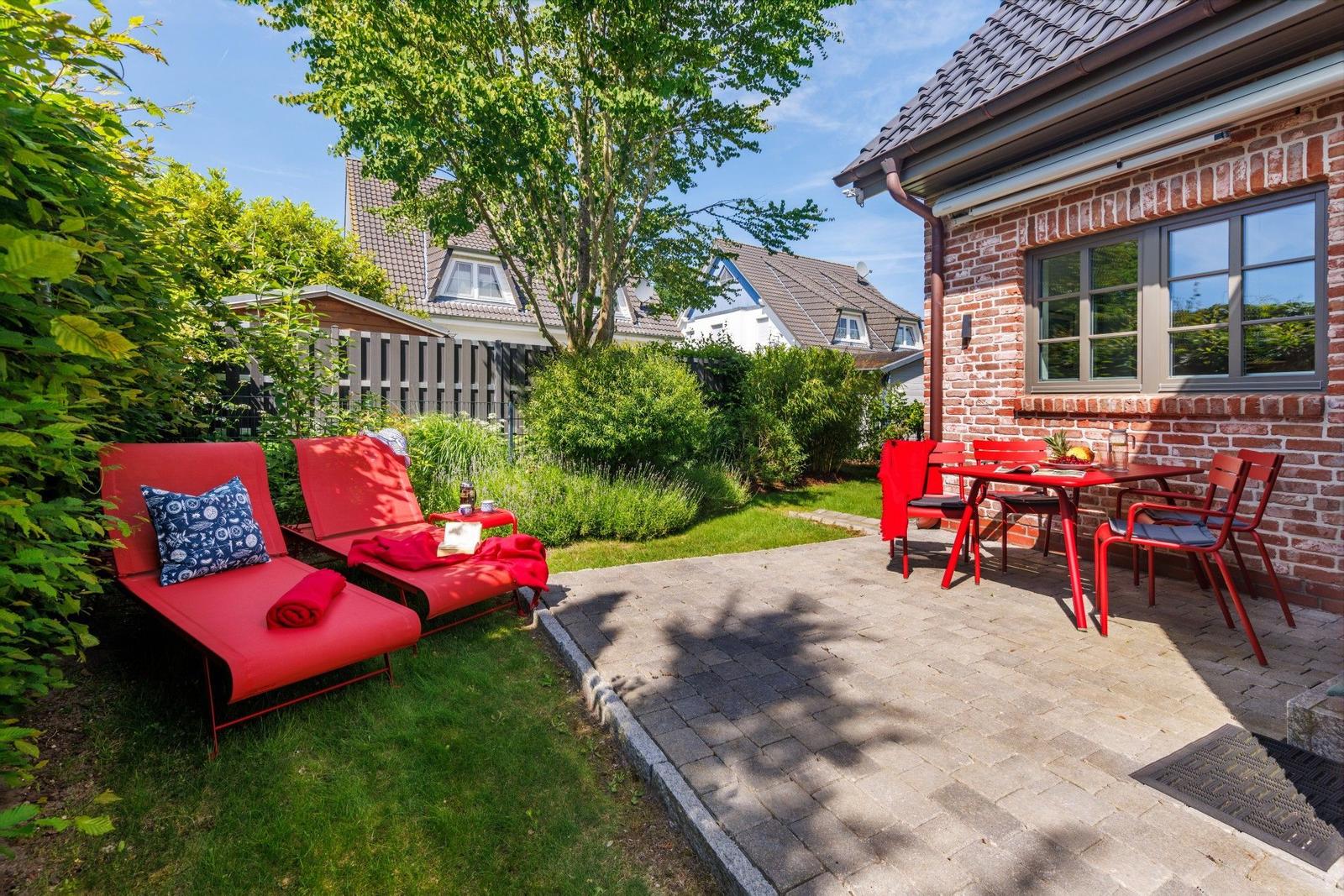Roter Liegestuhl und Tisch mit Stühlen auf gepflastertem Bereich neben Backsteinhaus.