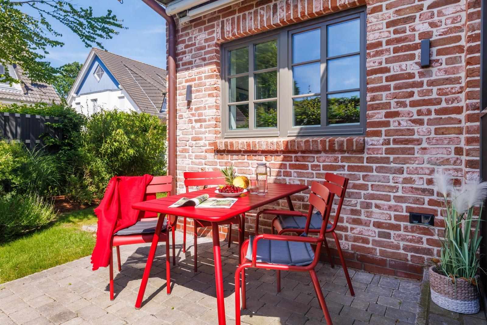Roter Tisch und Stühle auf Terrasse vor Backsteinhaus mit Fenster und Pflanze.