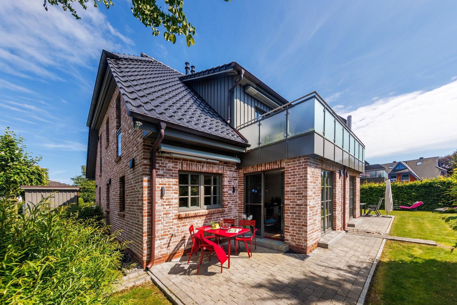 Zweistöckiges Haus mit Balkon, Terrasse und Garten. Rotes Tischset im Freien.
