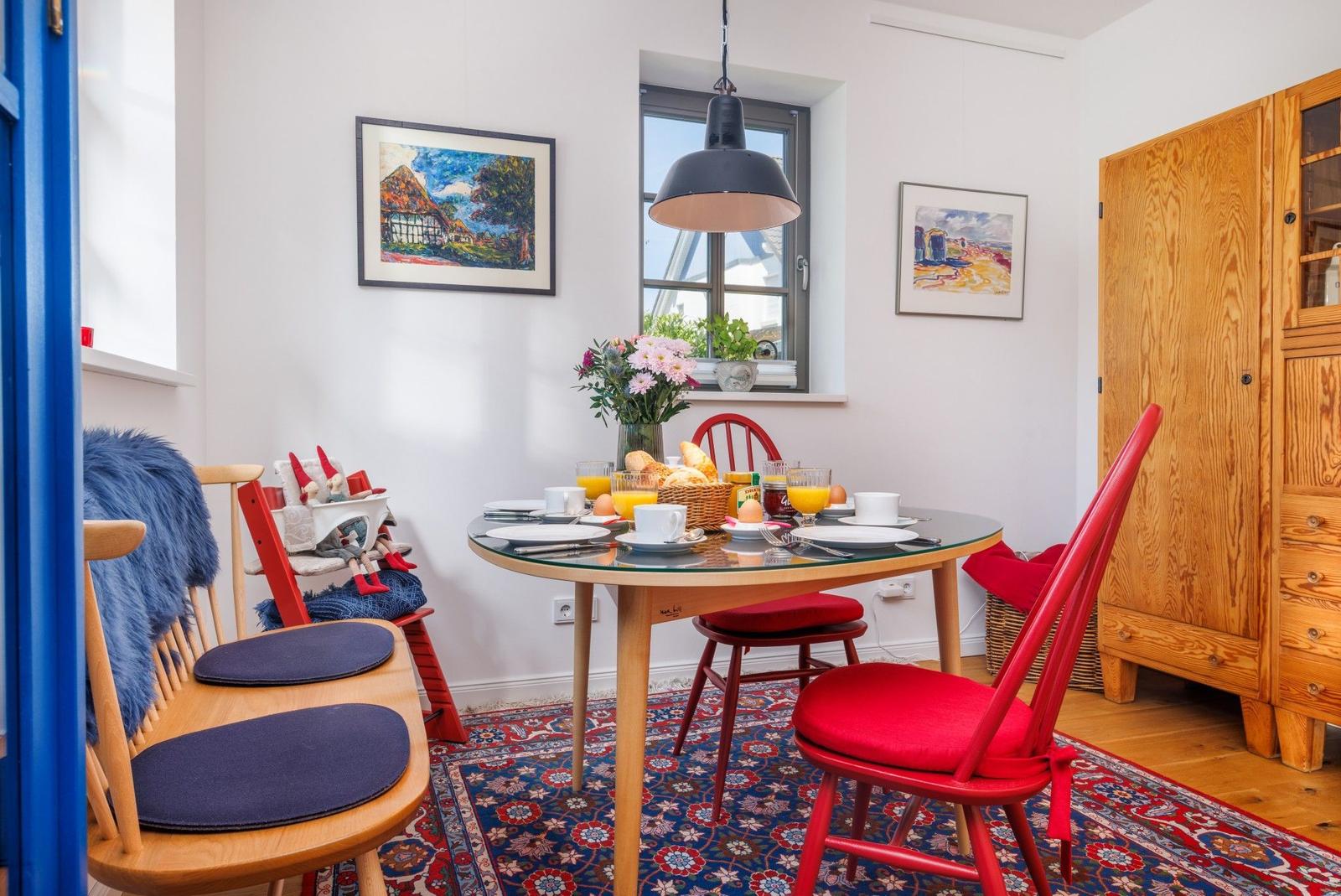 Esszimmer mit runden Tisch, roten Stühlen und Holzschrank. Blauer Teppich und Bilder an den Wänden.