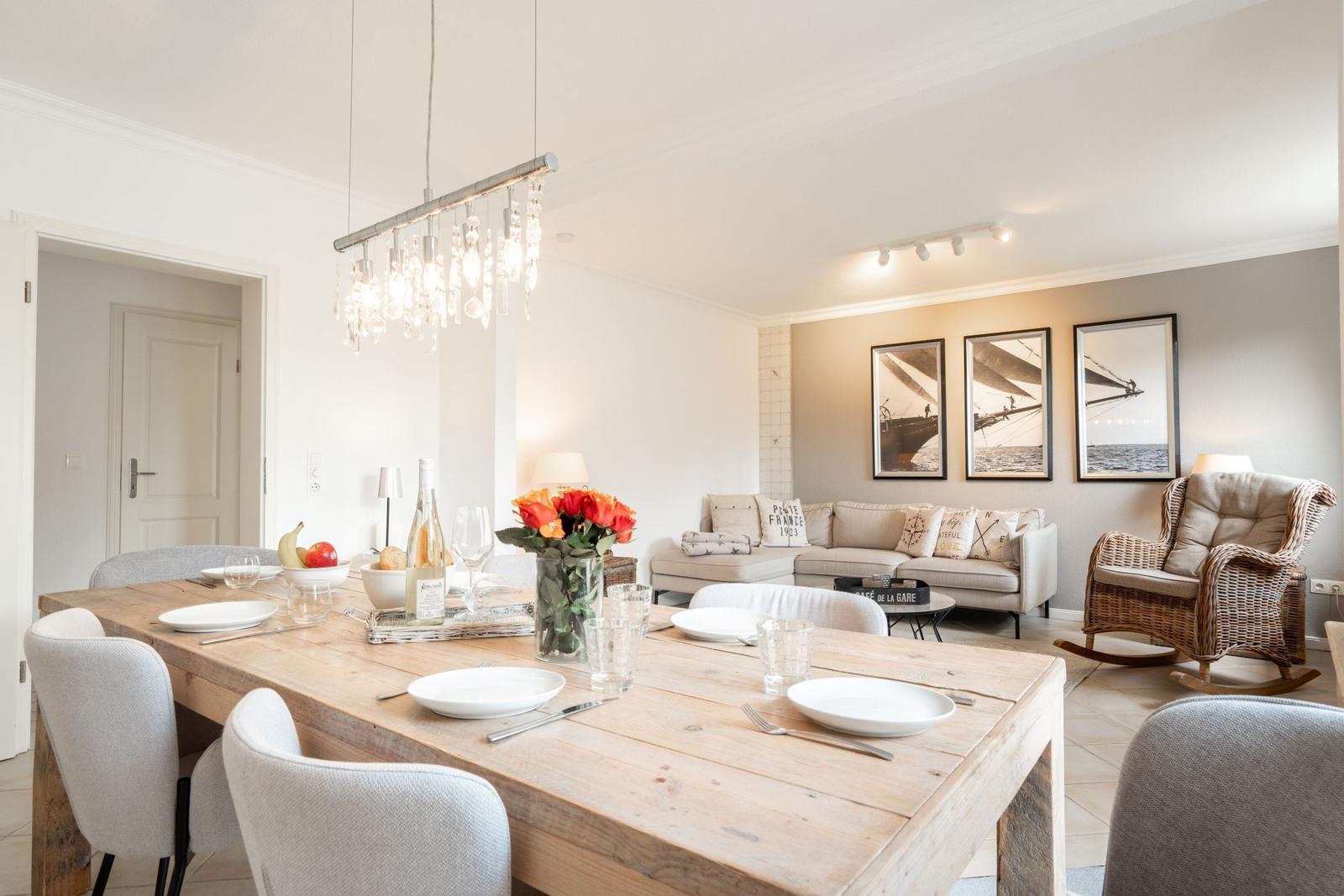 Dining room with wooden table and chairs. Living area with sofa and wall pictures in background.