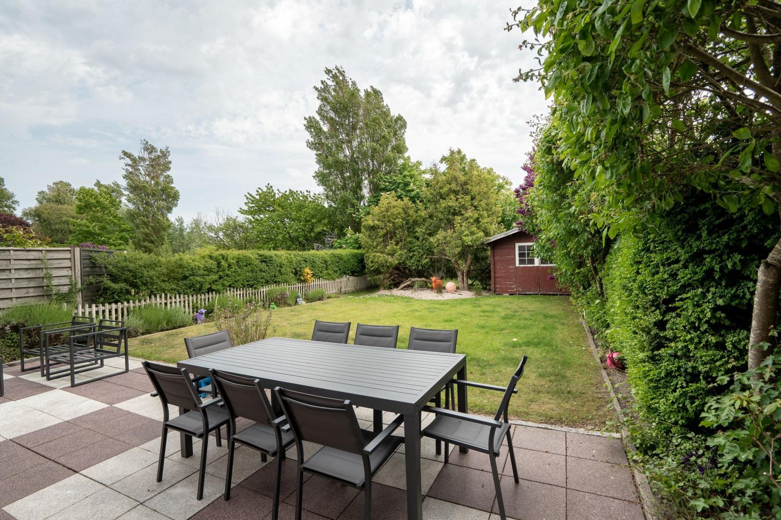 Terrace with table and chairs, lawn area, and small red garden shed.