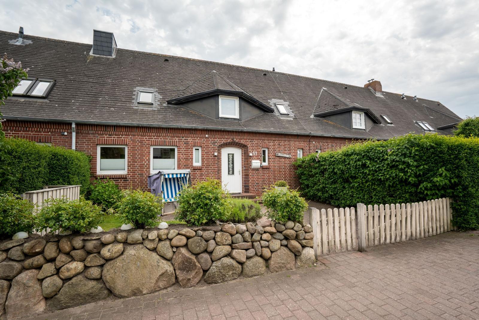 Red brick house with dormers and a well-kept garden with stone wall and wooden fence.