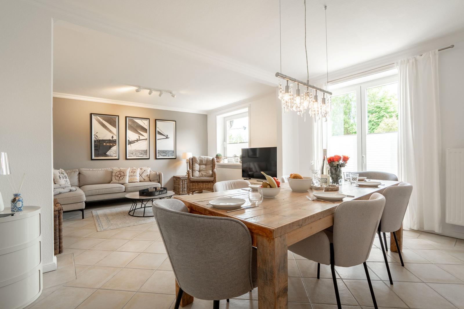 Dining room with wooden table and chairs. Living room with sofa and wall art.