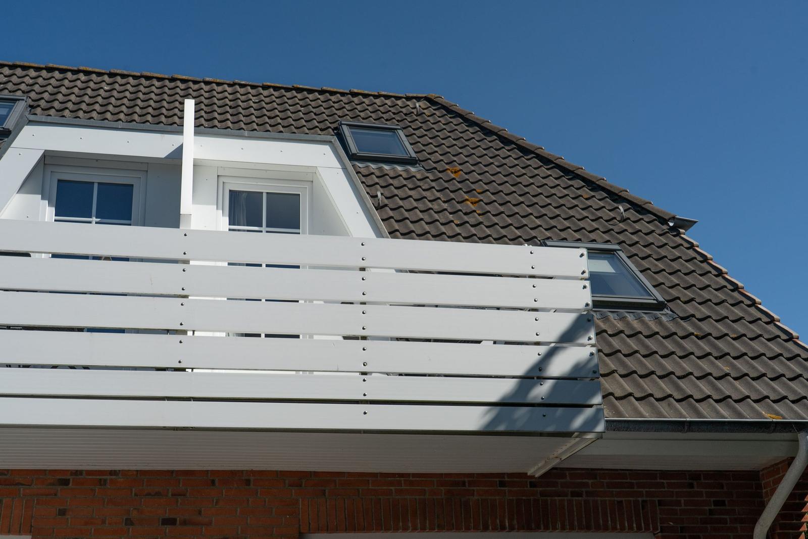 Dachterrasse mit weißen Holzgeländern und Dachfenstern an einem klaren Tag.