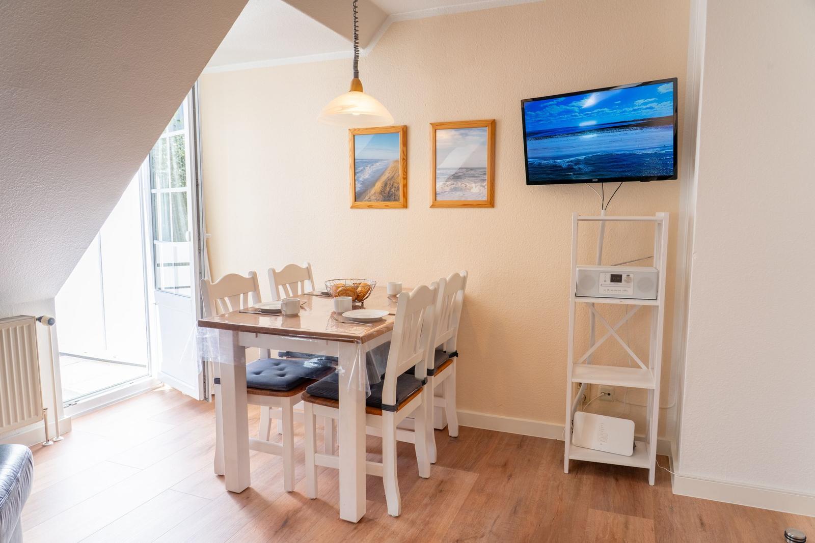 Esszimmer mit Tisch, Stühlen, TV und Fenster zur Terrasse.