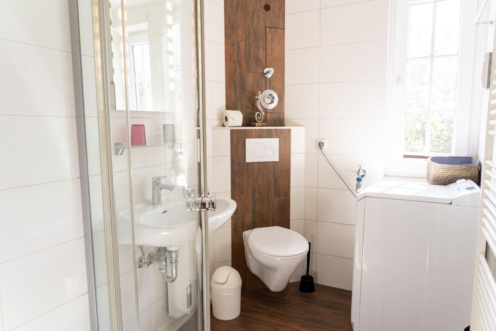 Badezimmer mit Dusche, Toilette und Waschmaschine. Holzwand und Fenster.