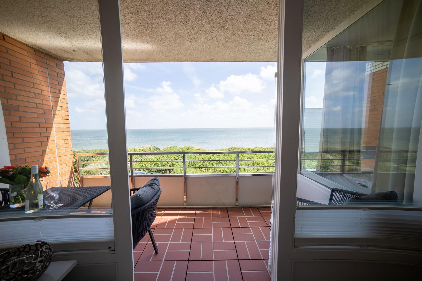 Terrace with sea view, table, chair, and flowers. Background: beach and sea.