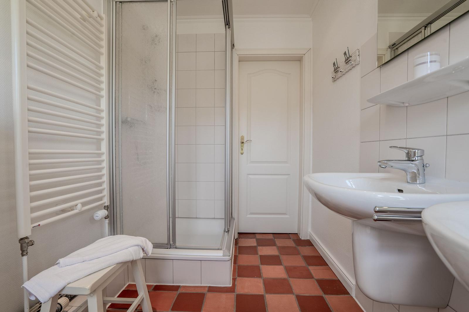 Badezimmer mit Dusche, Waschbecken und Heizkörper.