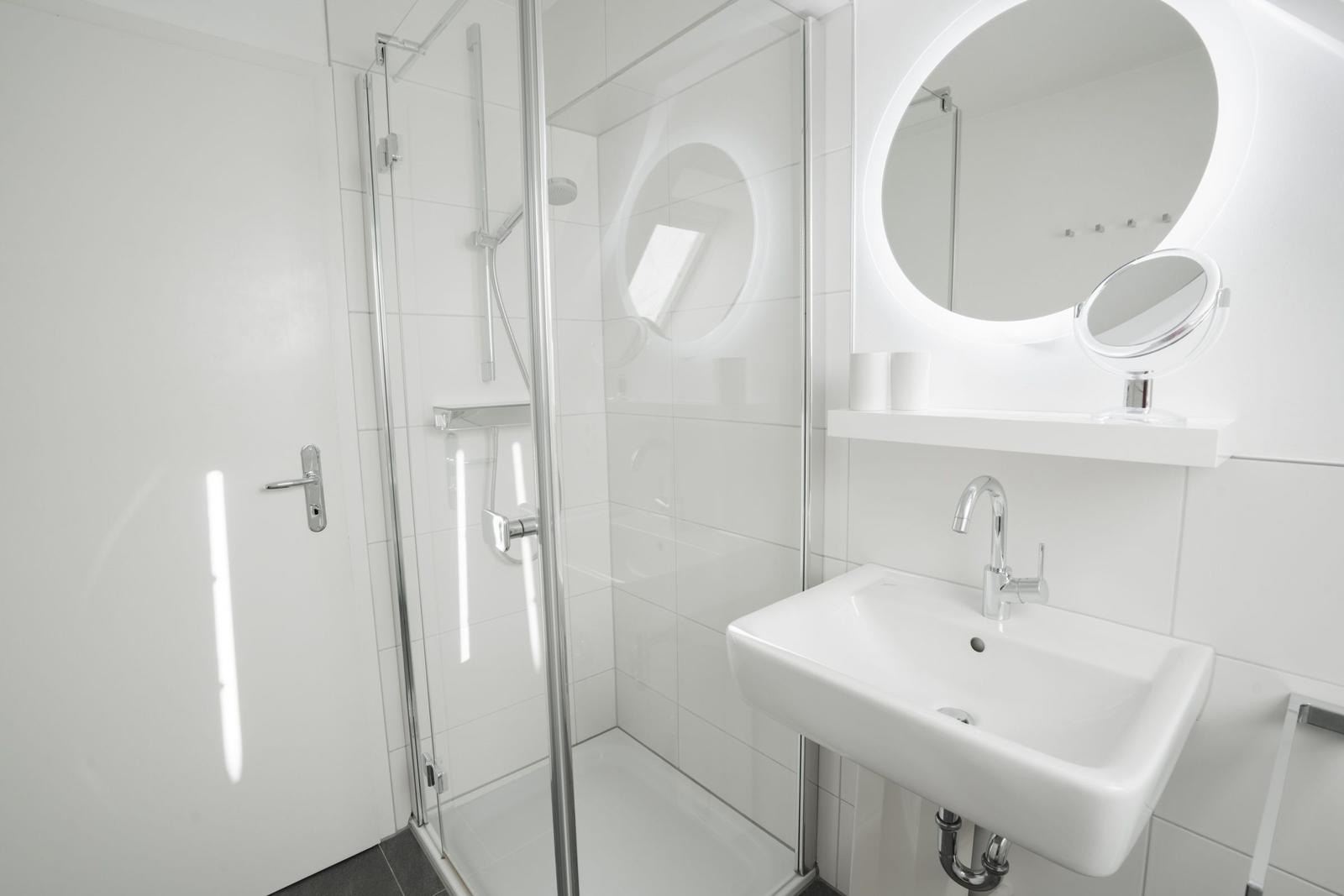 Badezimmer mit Dusche, Waschbecken und runden Spiegel