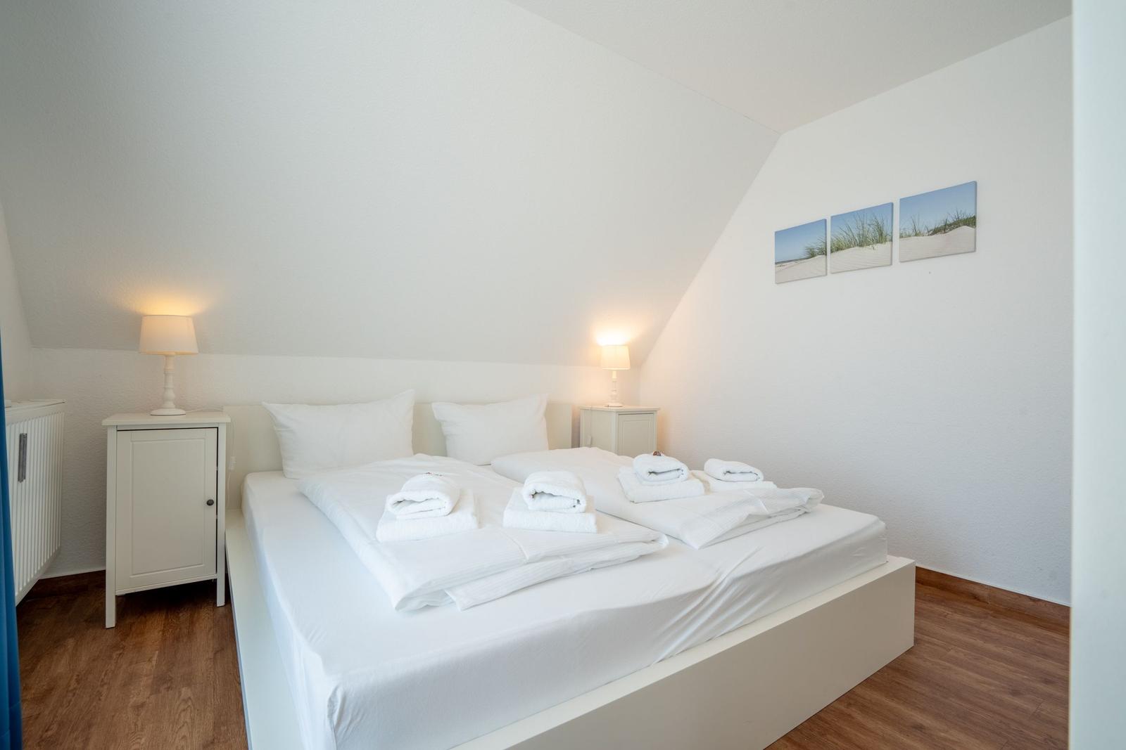 Schlafzimmer mit Doppelbett, zwei Nachttischen und Strandbildern an der Wand.