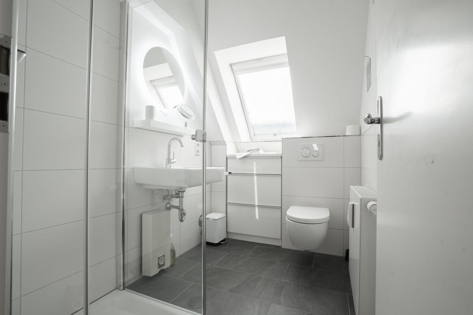 Badezimmer mit Dusche, Waschbecken und WC. Dachfenster sorgt für Tageslicht.
