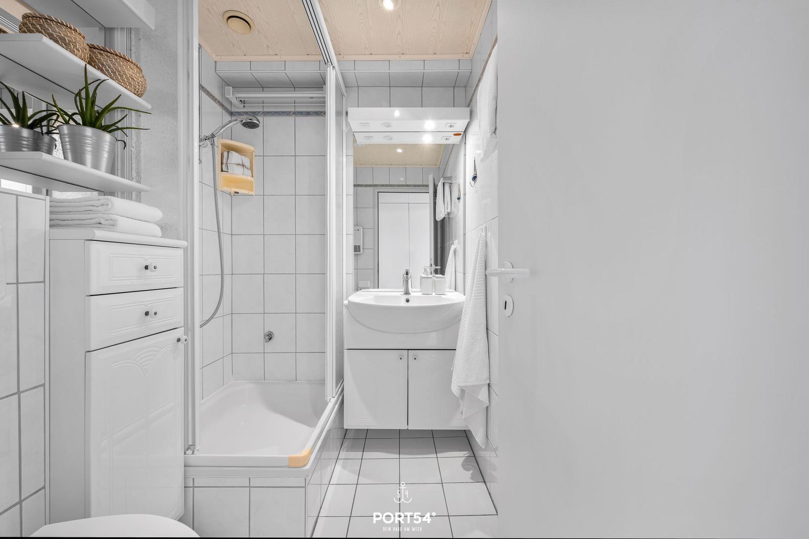 Bathroom with shower, sink, and cabinets. White tiles and wooden ceiling.