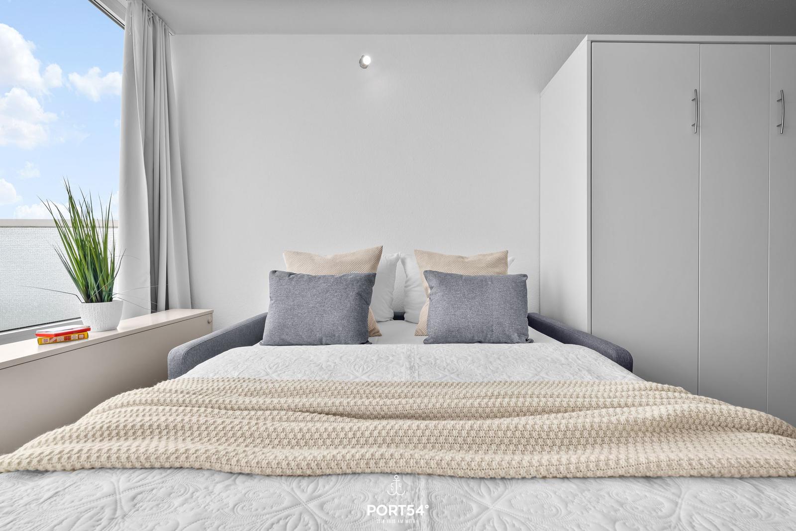 Bedroom with bed, wardrobe, and window overlooking water.