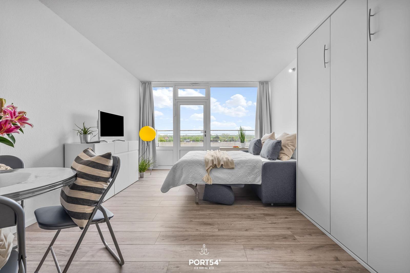 Bedroom with bed, TV, and balcony view. Wooden floors and white closet.