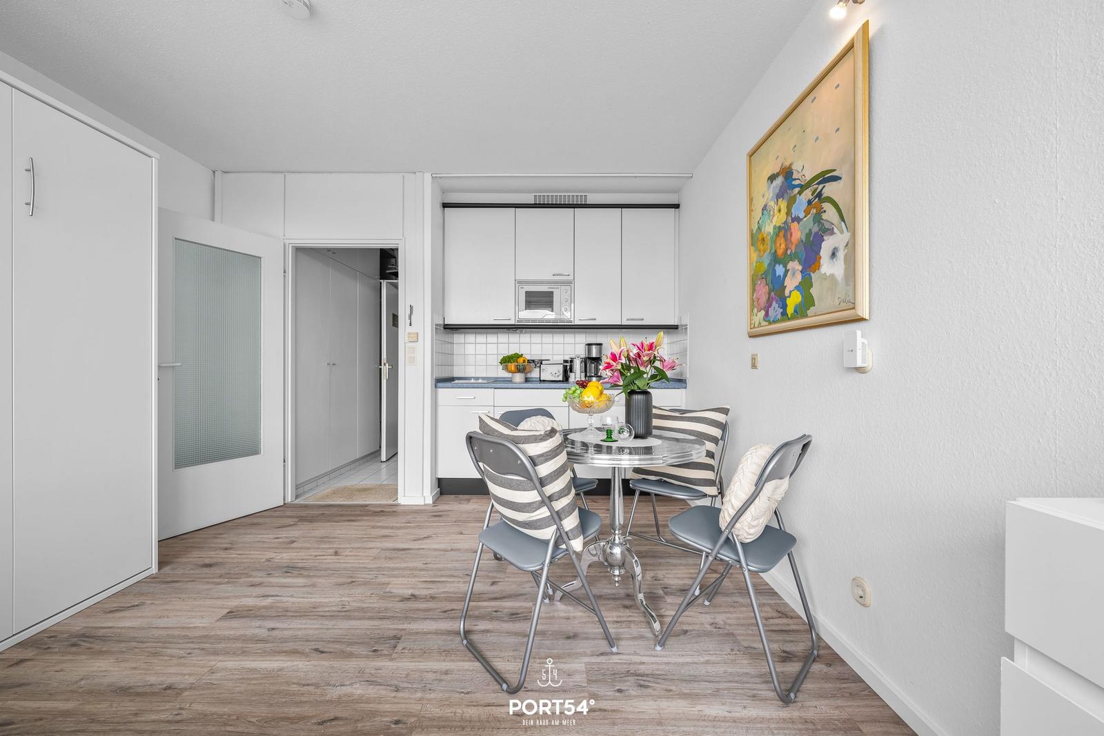 Kitchen with dining table and chairs. Wall art and wooden floor visible.