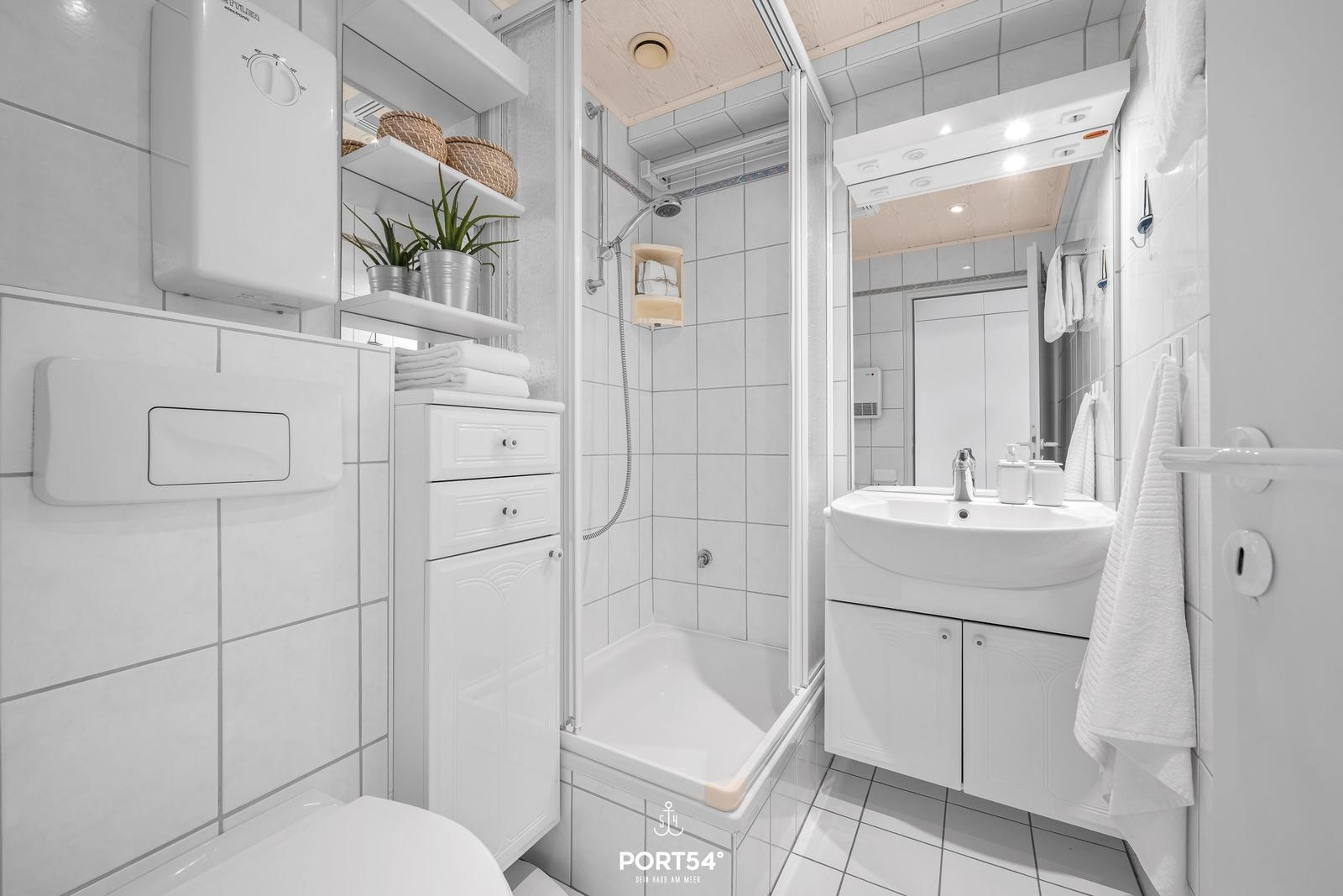 Bathroom with shower, sink, and toilet. White tiles and fixtures.