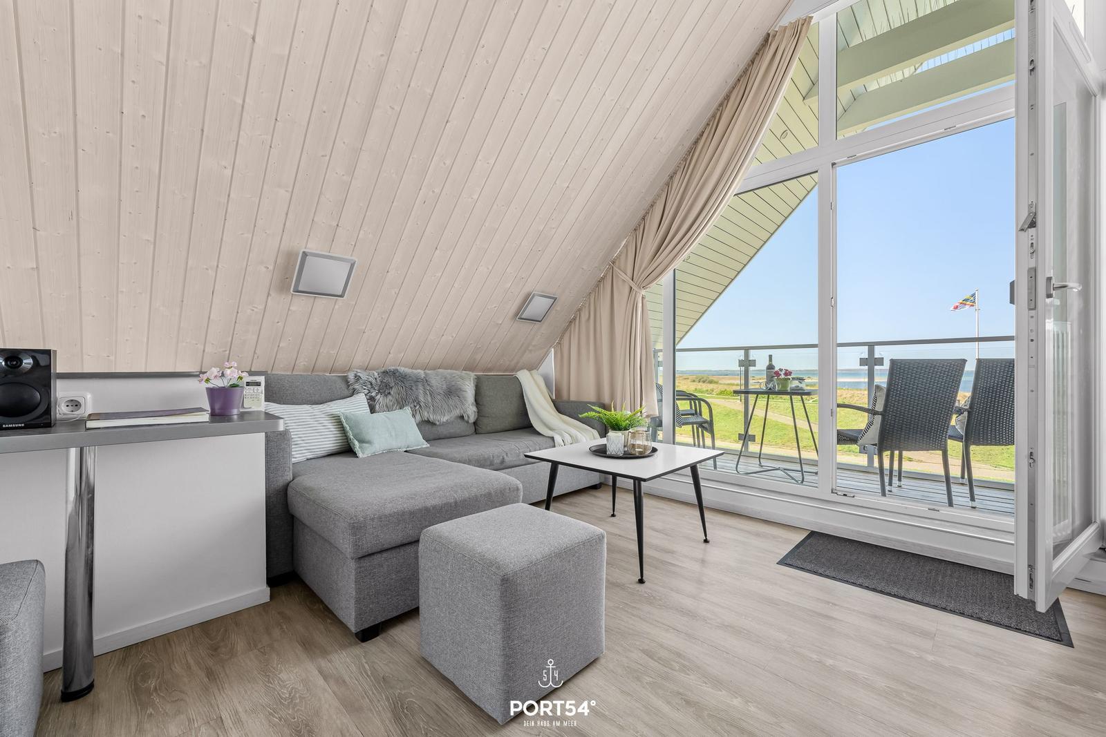 Wohnbereich mit Sofa, Tisch und Blick auf Balkon mit Meerblick.
