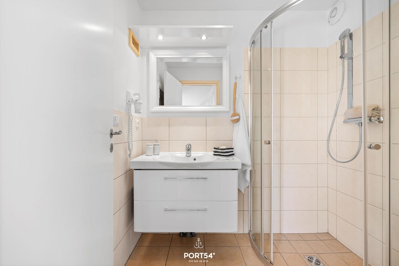Badezimmer mit Dusche, Waschbecken und Spiegel. Fliesenwand und Bodenfliesen.