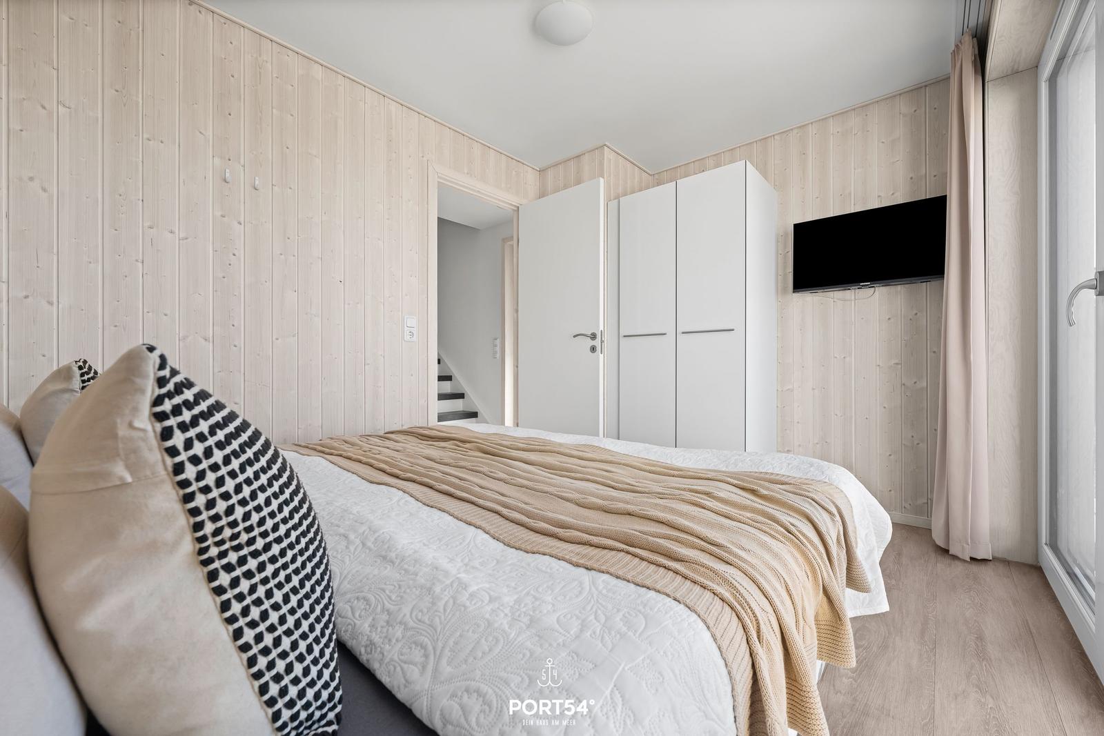 Schlafzimmer mit Bett, Kleiderschrank und TV an der Wand.