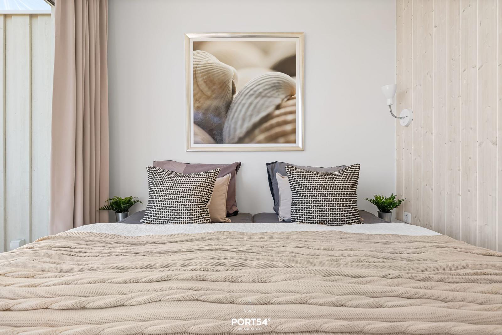 Schlafzimmer mit Bett, Kissen und Wandbild mit Muscheln.