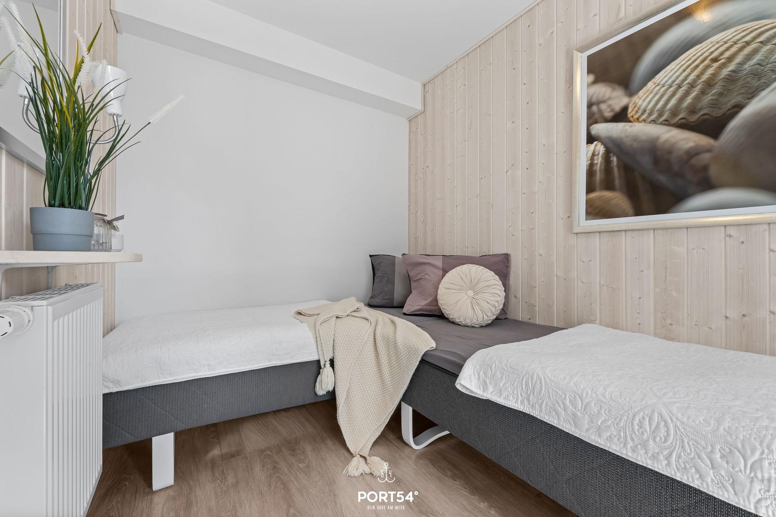 Zwei Betten mit weißen Bettwäschen und Kissen an einer Holzwand mit Meeresmuschel-Bild.