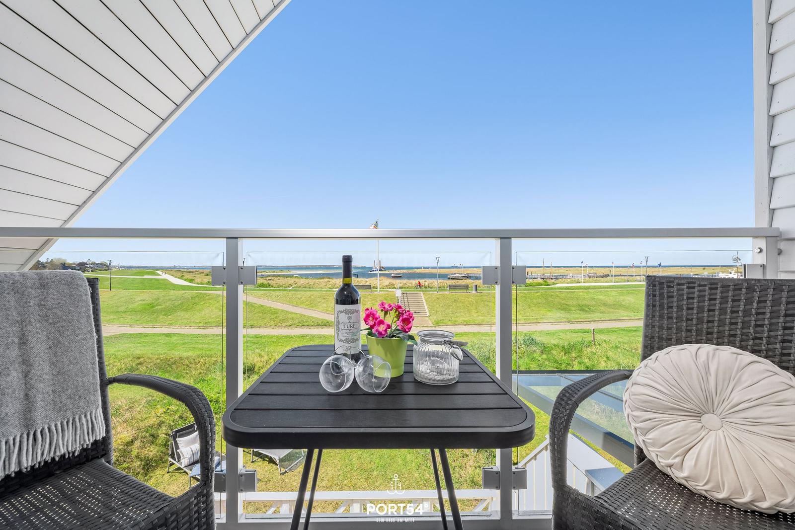 Terrasse mit Tisch, Stühlen und Blick auf Grünflächen und Wasser.