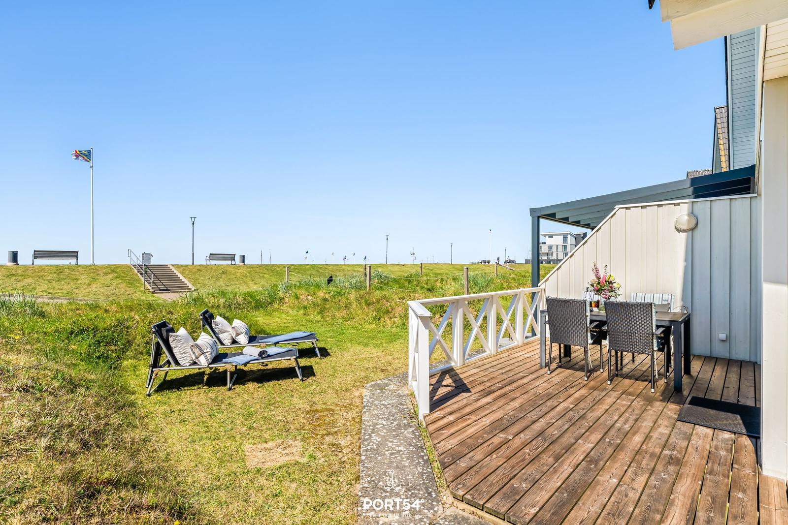 Terrasse mit Tisch und Stühlen. Außenbereich mit Liegestühlen und Grünfläche.
