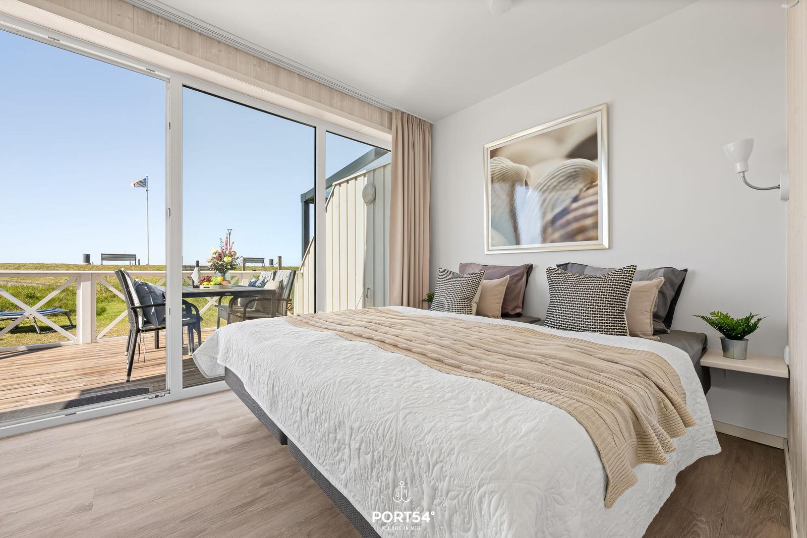 Schlafzimmer mit Blick auf Balkon und Garten. Bett mit Kissen und Decke. Wandbild und Pflanze.