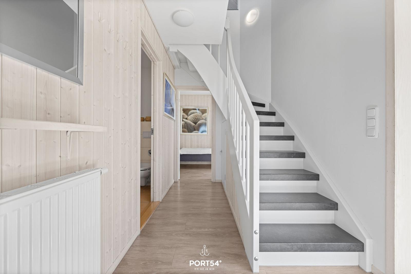 Hausflur mit Treppe, Holzwand und Blick in Schlafzimmer und Badezimmer.