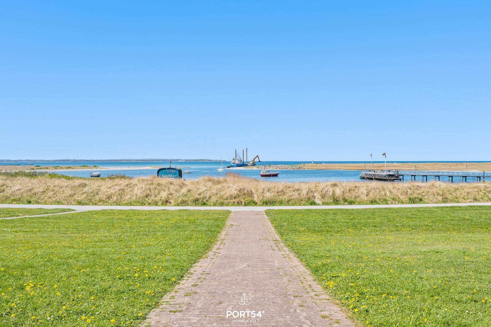 Pfad durch Grasland zum Hafen mit Booten und Steg.