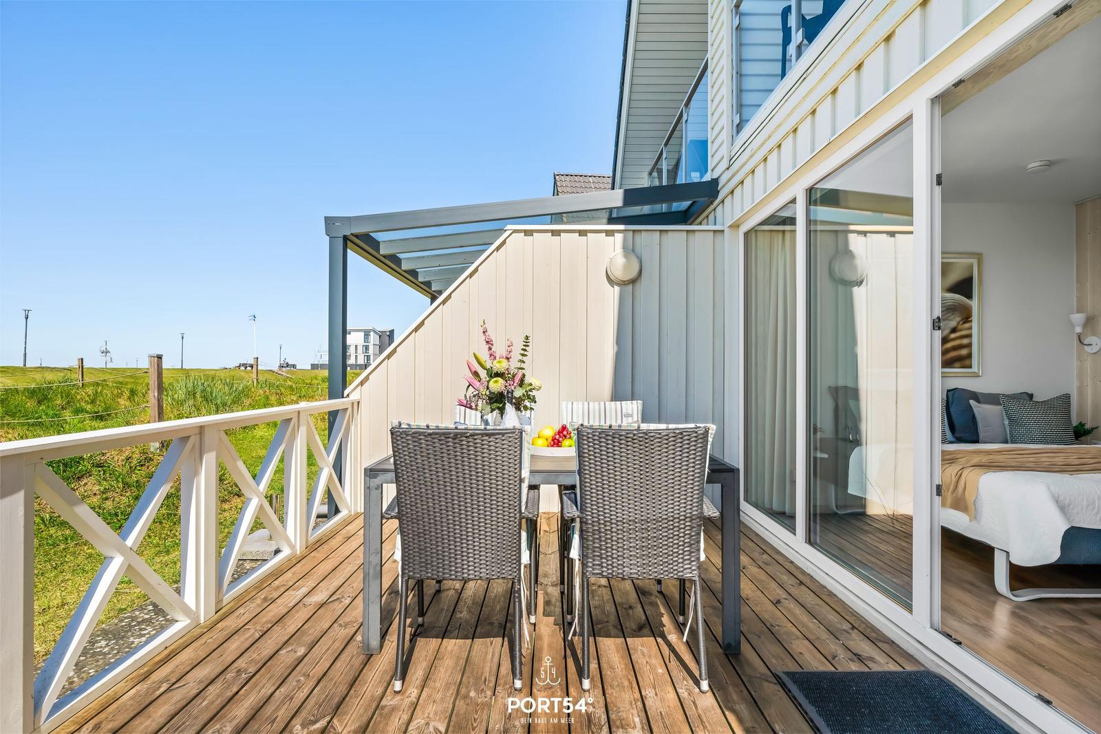 Terrasse mit Tisch und Stühlen, Blick auf Grünland und Schlafzimmer im Hintergrund.