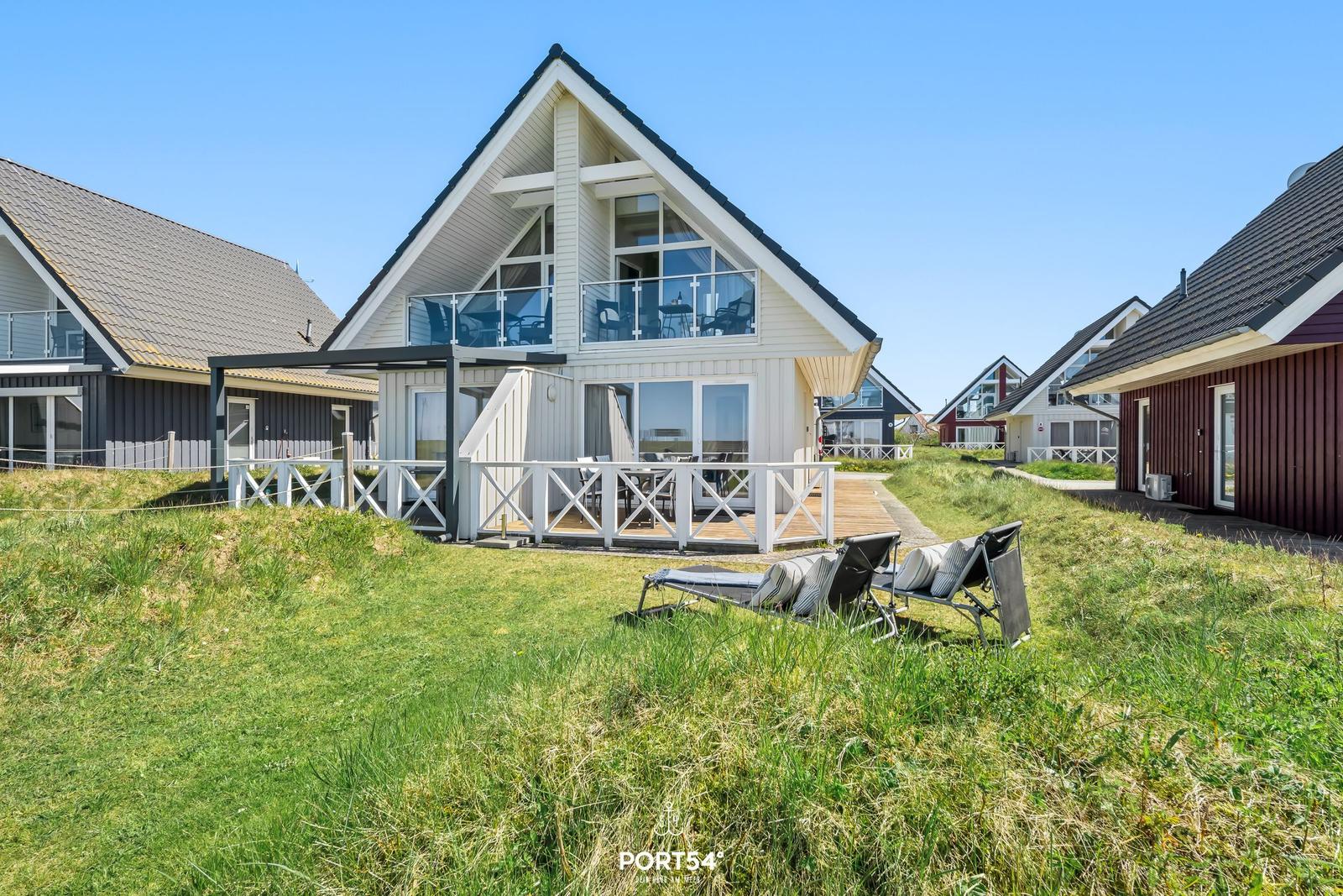Haus mit Balkon und Terrasse, umgeben von Gras und anderen Häusern.