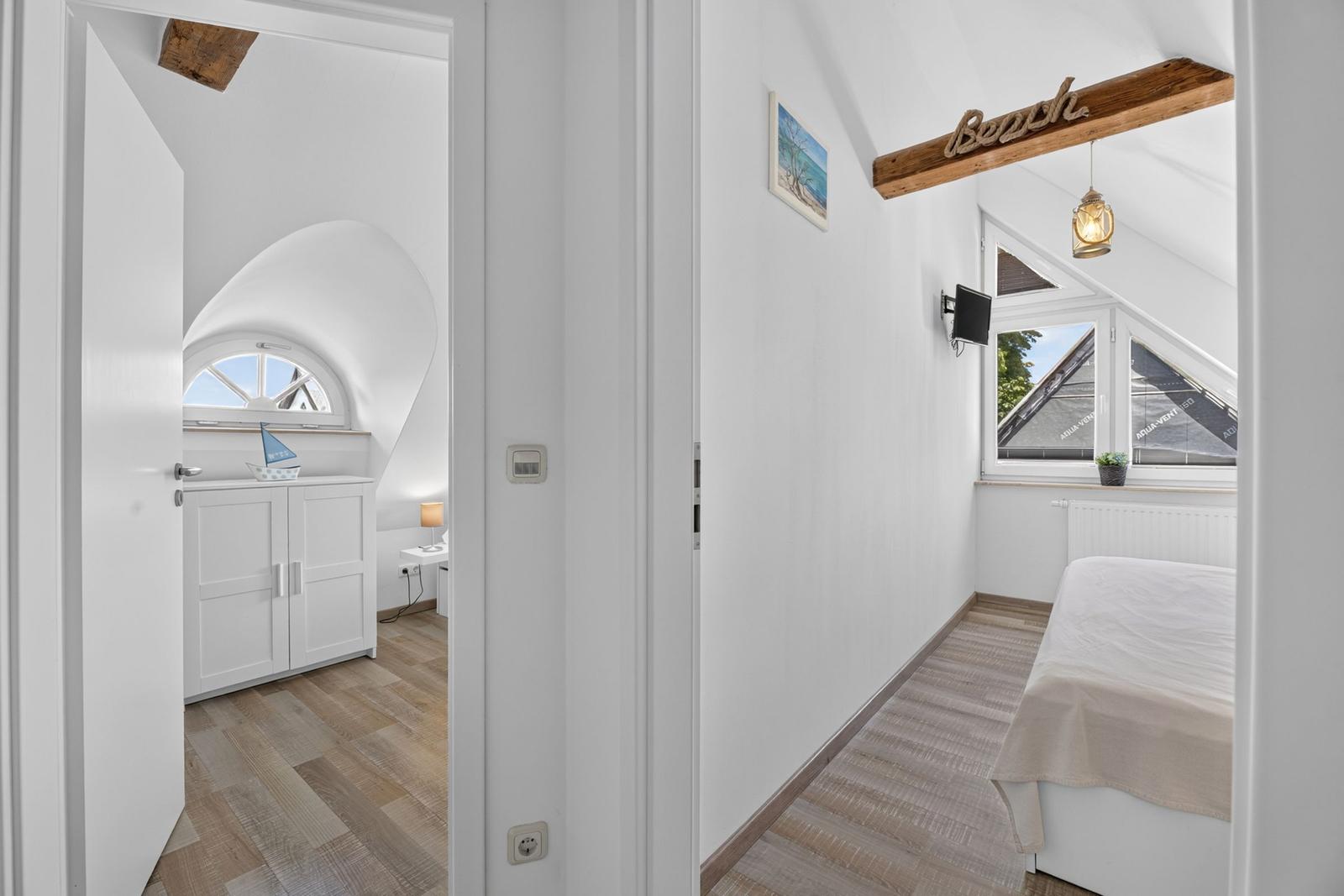 Schlafzimmer mit Bett, Fenster und Holzdecke. Nebenraum mit Schrank und Bogenfenster.