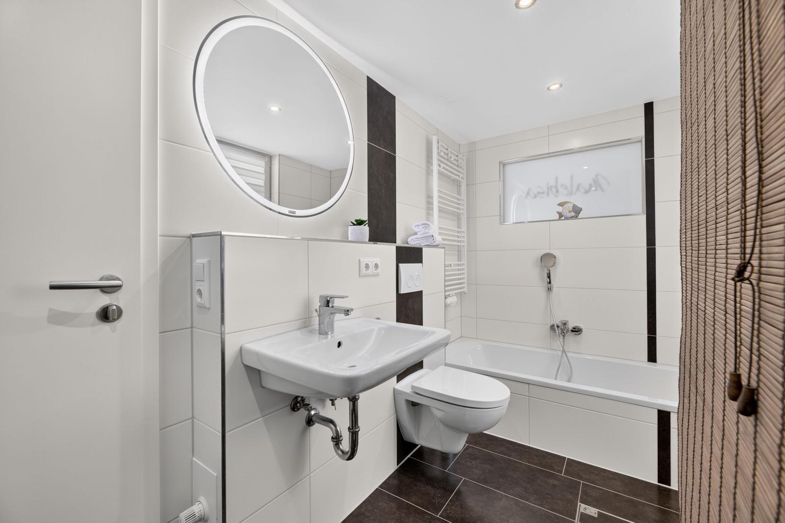 Badezimmer mit Badewanne, WC, Waschbecken und runden Spiegel.