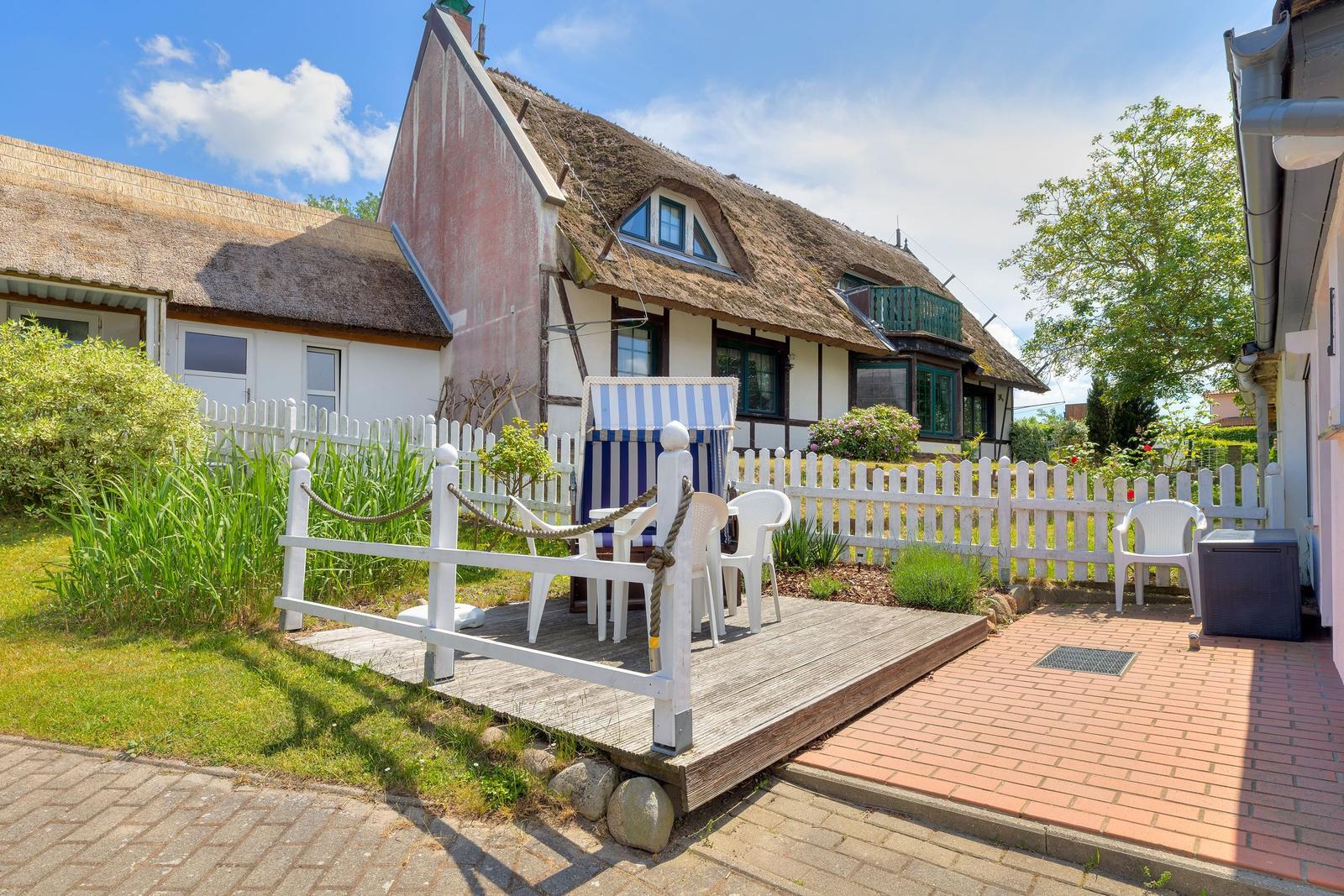Haus mit Strohdach, weißer Zaun und Terrasse mit Liegestuhl und Tisch.