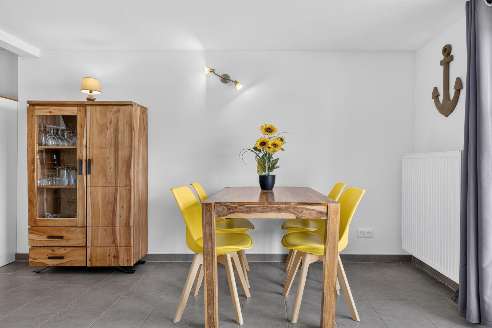 Esszimmer mit Holztisch, vier gelben Stühlen und einem Holzschrank. An der Wand hängt ein Anker.