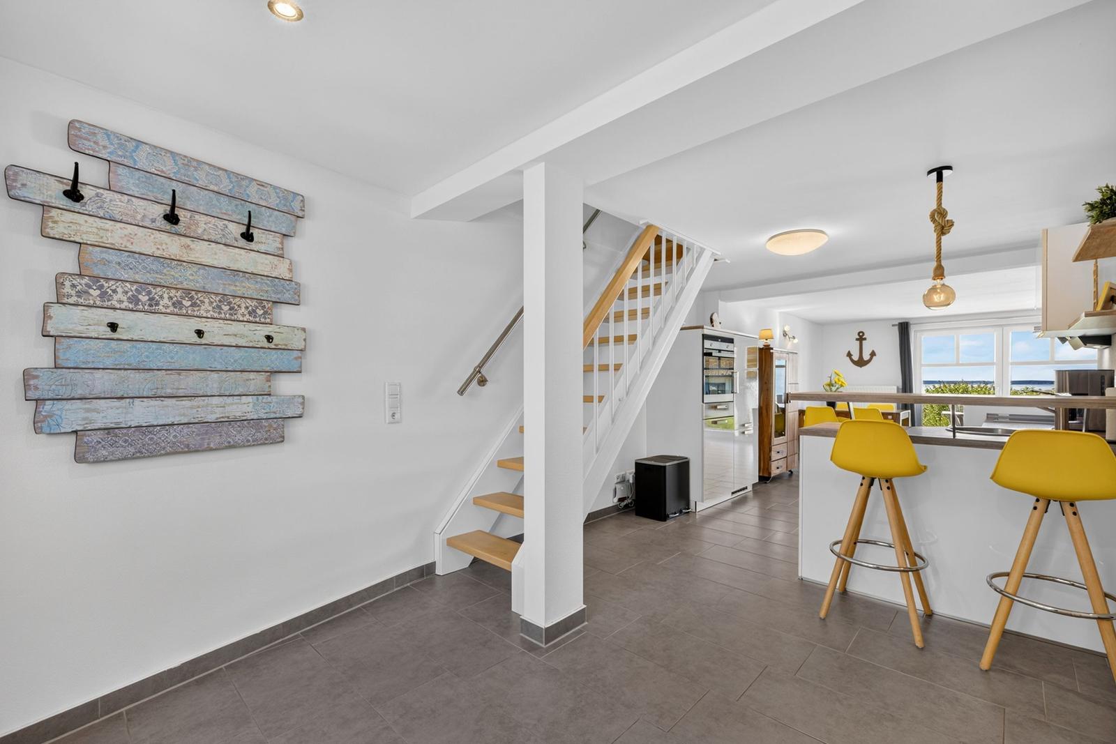Haus mit Kücheninsel, gelben Barhockern und Holztreppe zur oberen Etage.