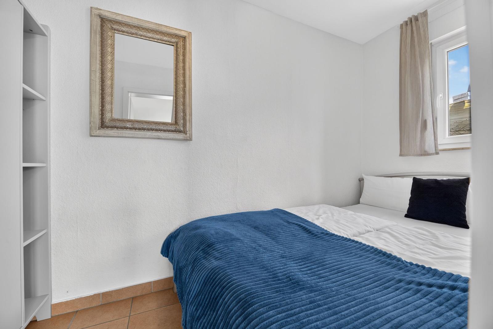 Schlafzimmer mit Bett, Spiegel und Fenster.