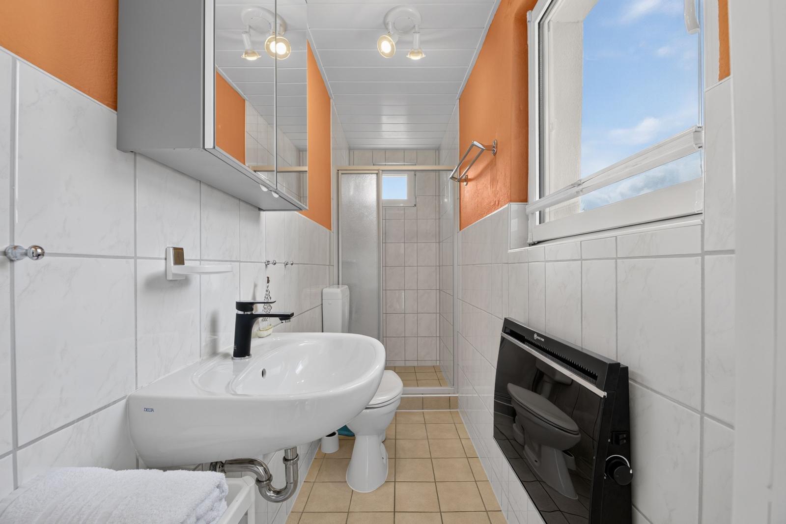 Badezimmer mit Waschbecken, Toilette und Dusche. Fenster und Wandverkleidung.