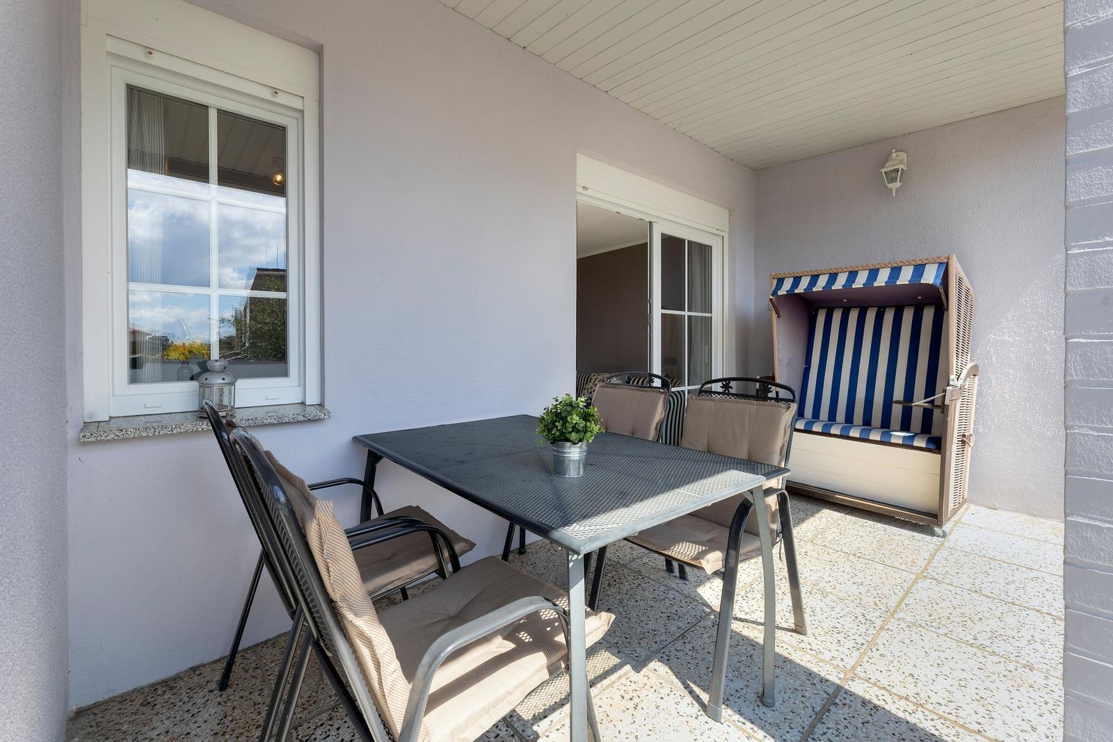Terrasse mit Tisch, Stühlen und Strandkorb. Fenster und Glastür führen ins Haus.