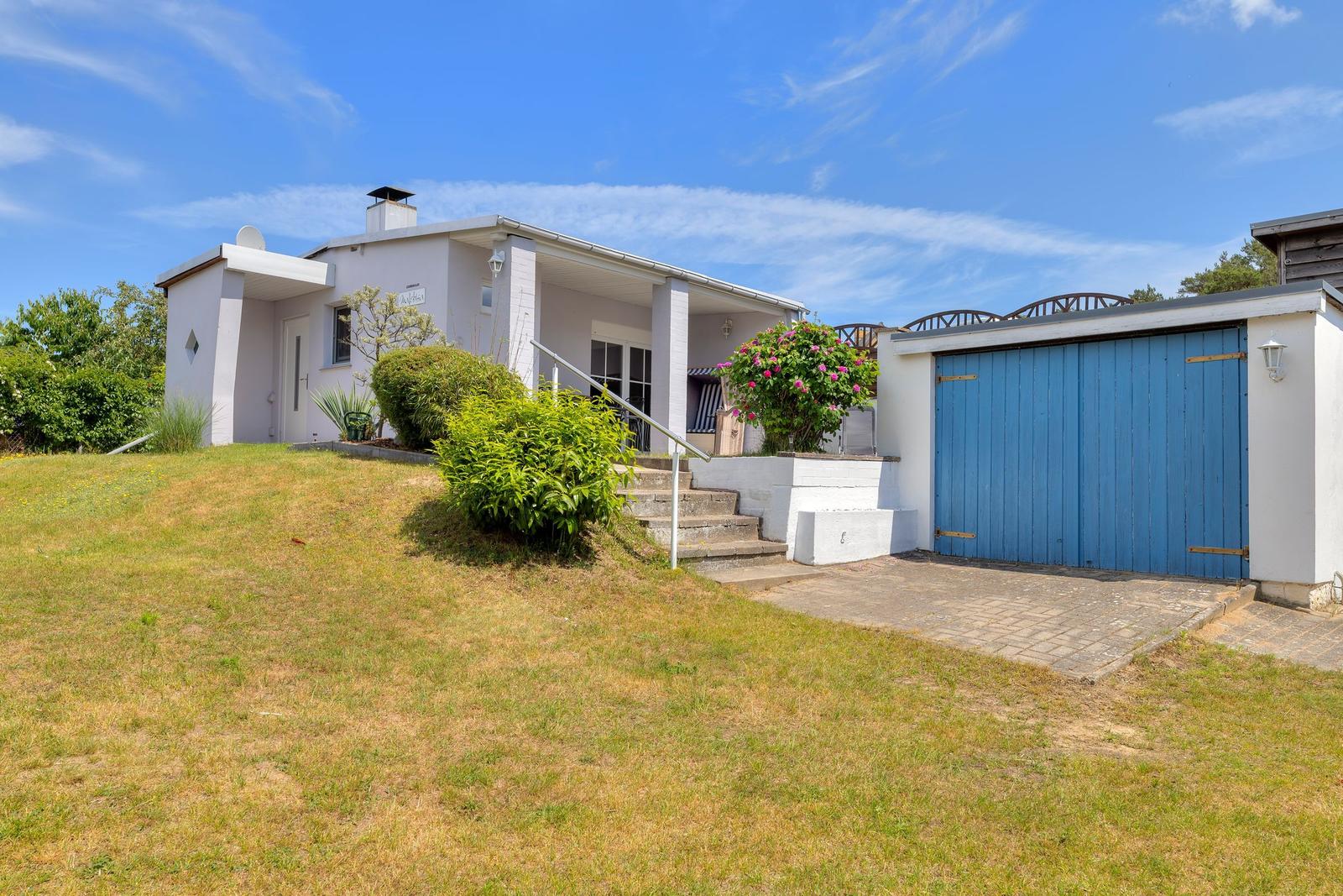 Wohnhaus mit Garage, Terrasse und Garten unter blauem Himmel.